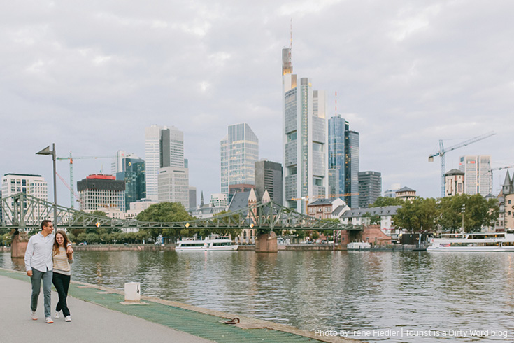 Strolling along the Main riverfront with the Eiserner Steg bridge and 'Mainhattan' skyline of Frankfurt am Main in the background | Photo by Irene Fiedler for Tourist is a Dirty Word Blog